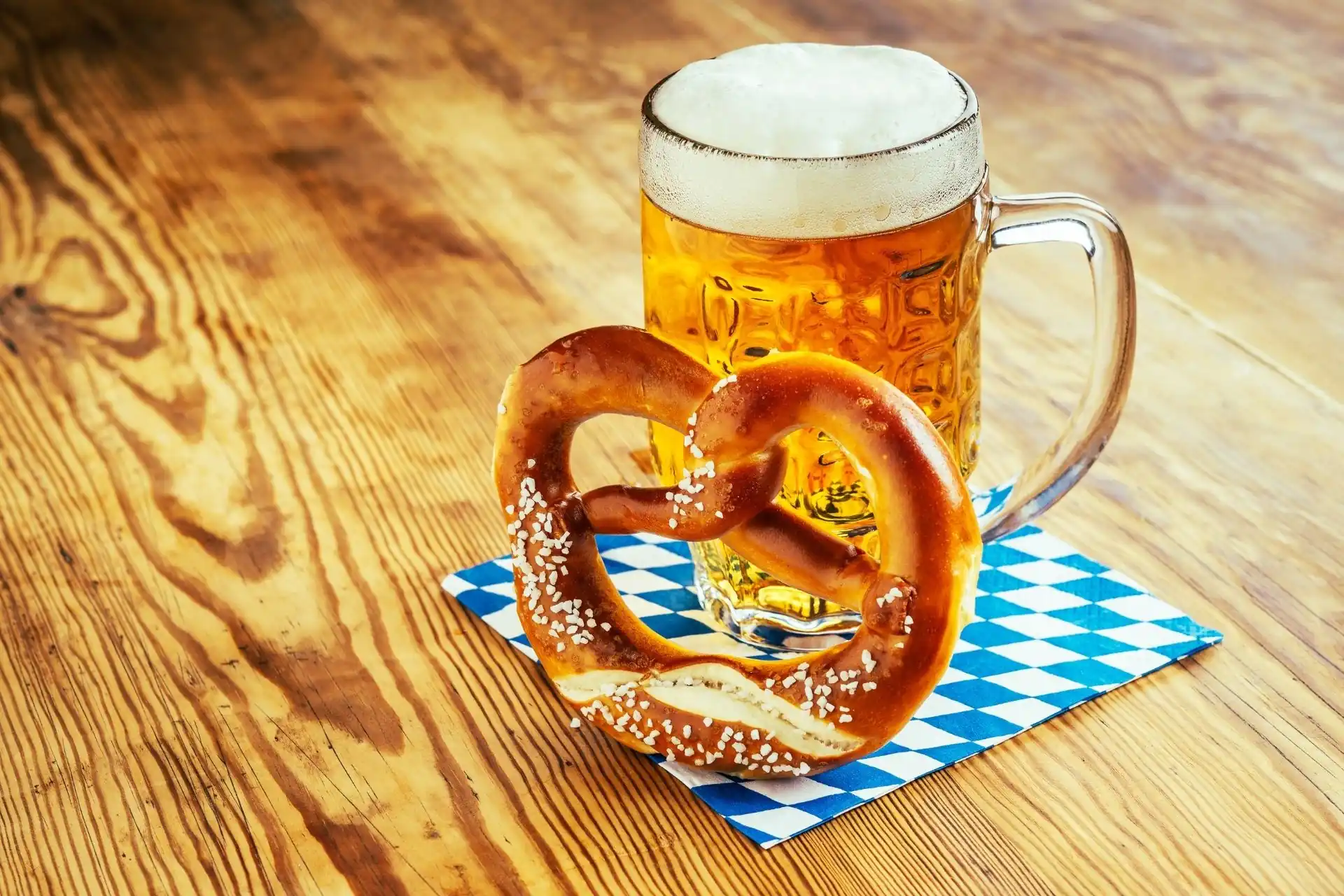 Bavarian soft pretzel and mug of Oktoberfest-style beer on a blue-and-white checkered napkin