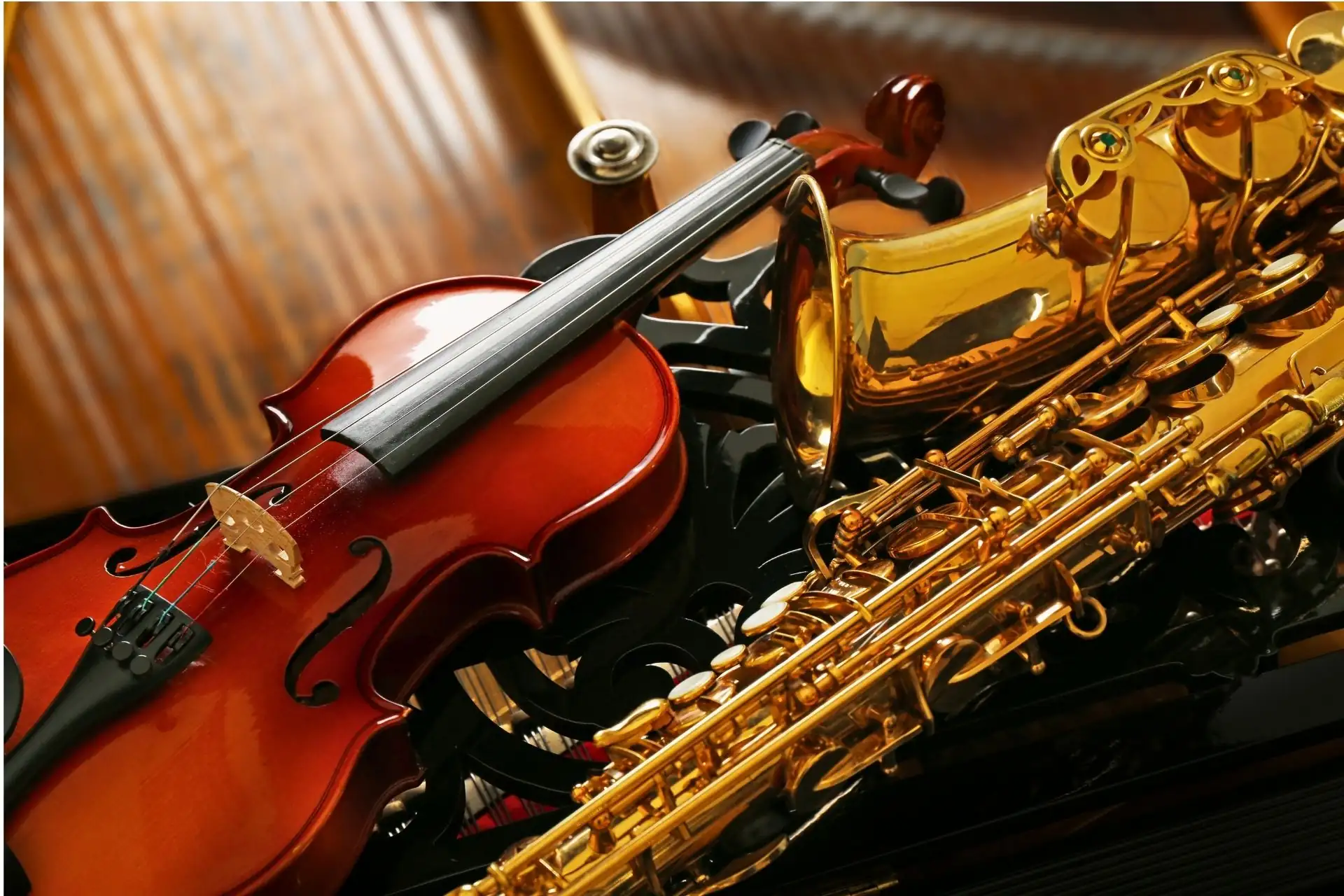 Close-up of a wooden violin and a polished brass alto saxophone resting together on an ornate black piano music desk.
