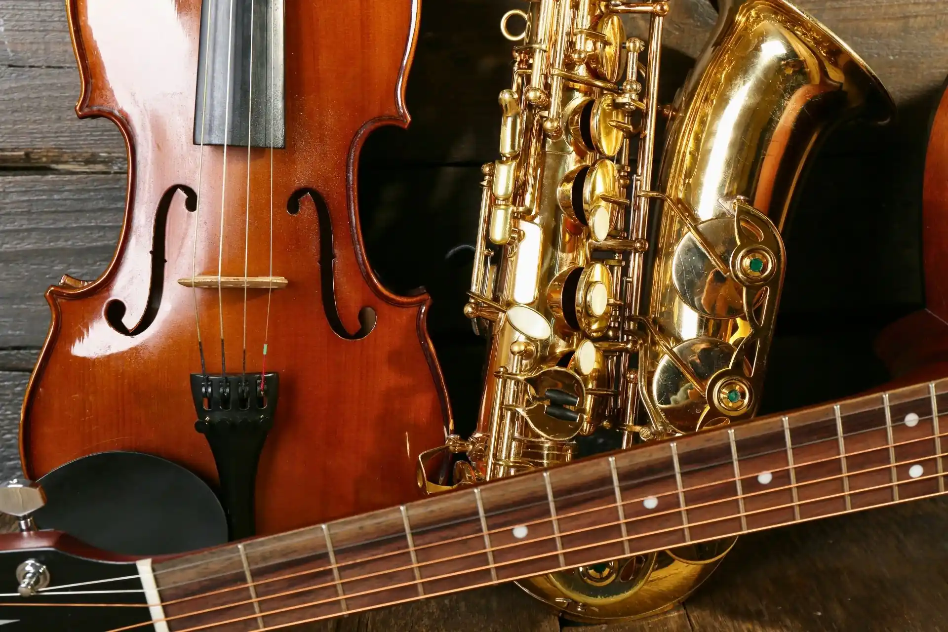 Close-up of a wooden violin and a polished brass alto saxophone resting together on an ornate black piano music desk.