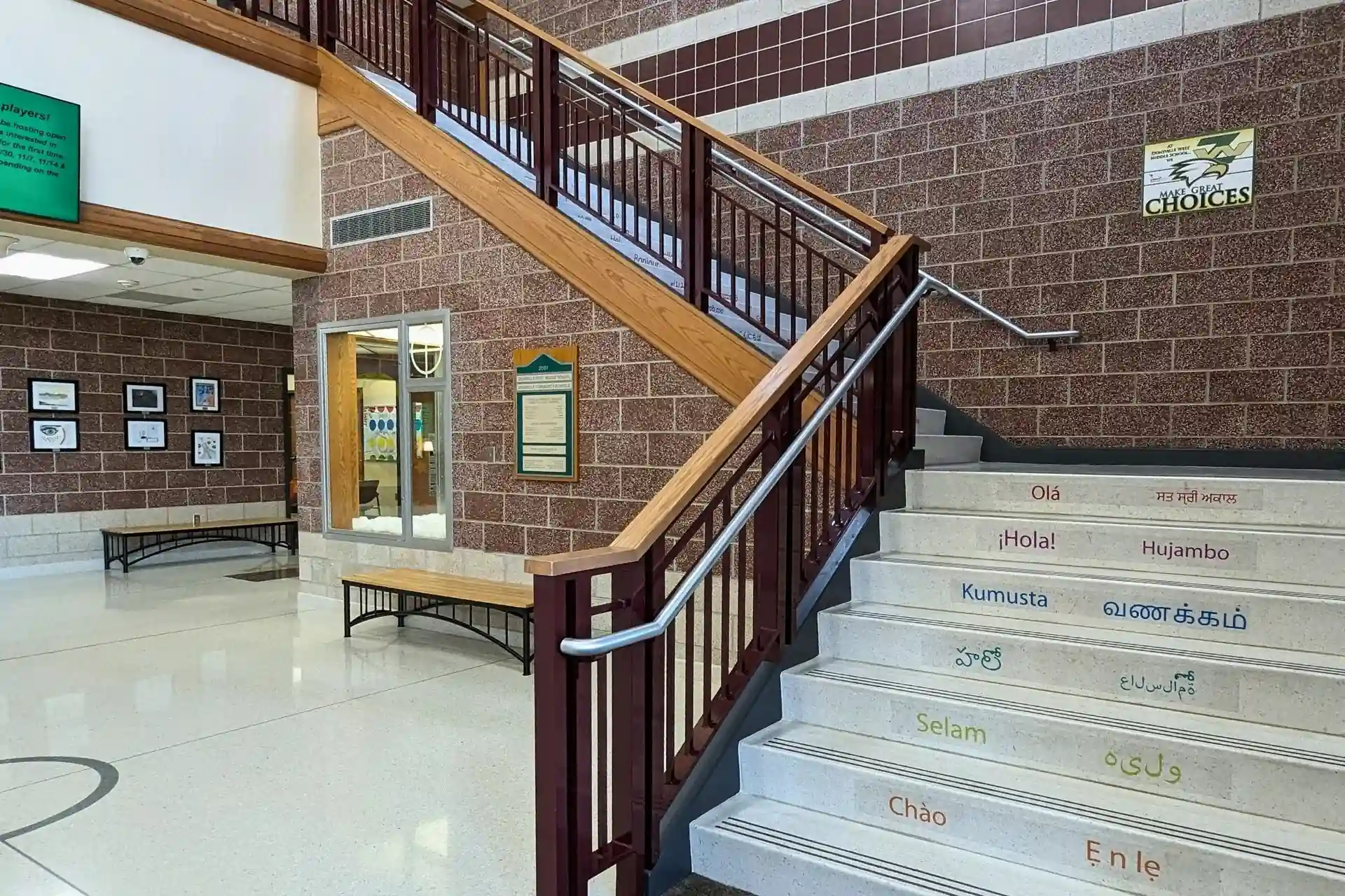 Interior lobby and central staircase at a Zionsville Community Schools facility featuring multilingual welcome greetings printed on the stair risers.