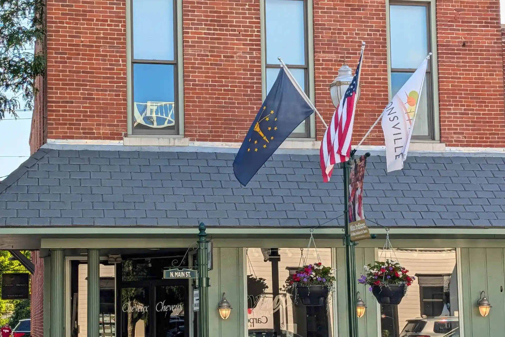Indiana state flag, American flag, and Zionsville town flag flying on a lamppost outside storefronts on Main Street in downtown Zionsville, Indiana.