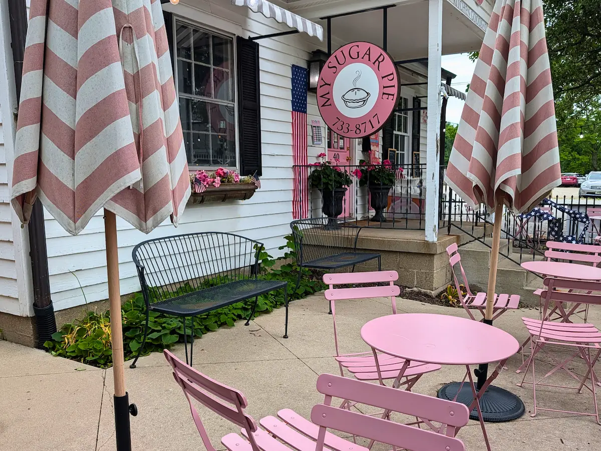 The exterior of My Sugar Pie shop in Zionsville, featuring its circular pink sign, pink outdoor patio seating, and striped umbrellas.