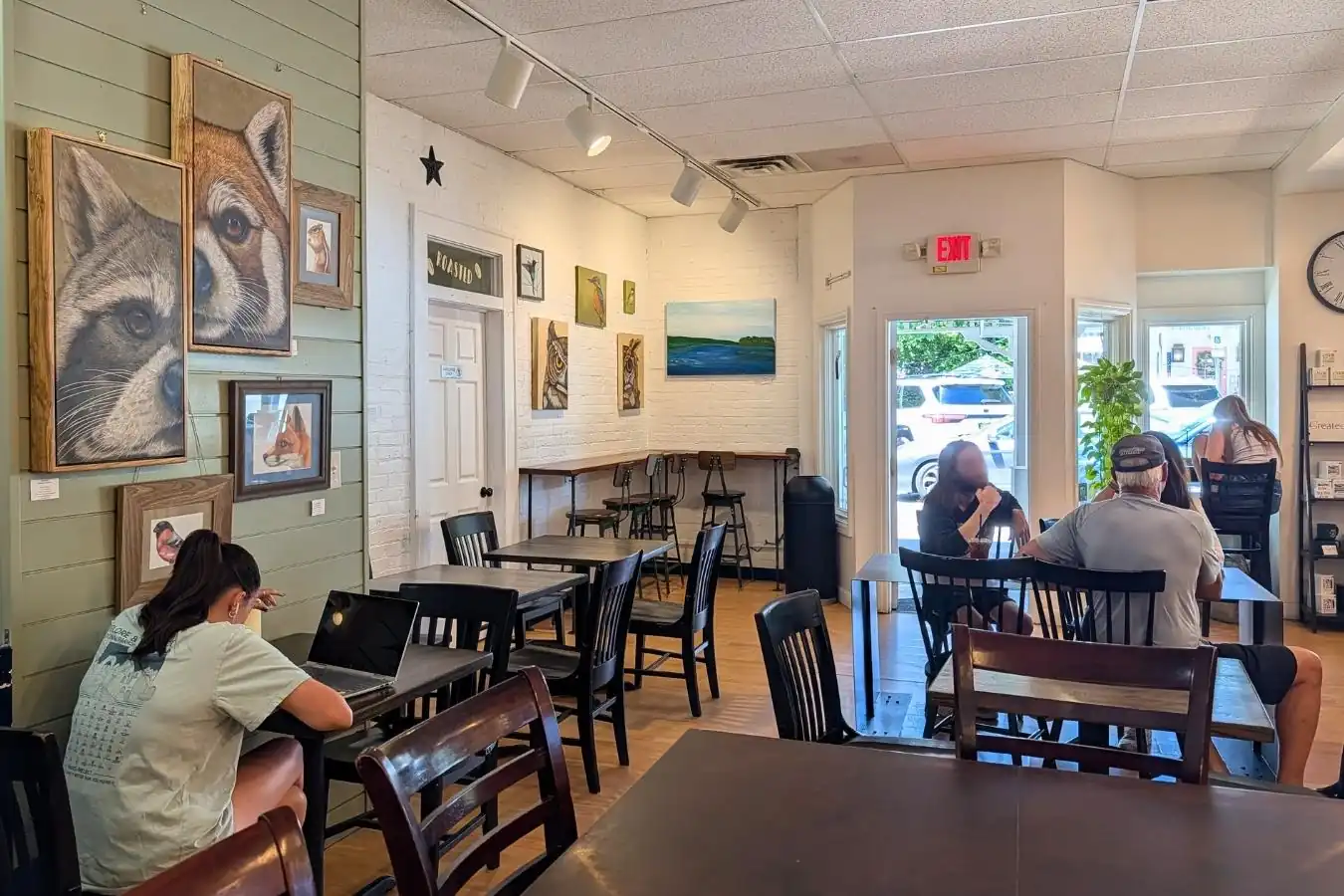 The interior dining room of Roasted in the Village coffee shop in Zionsville, showing customers at wooden tables and animal artwork on the walls.