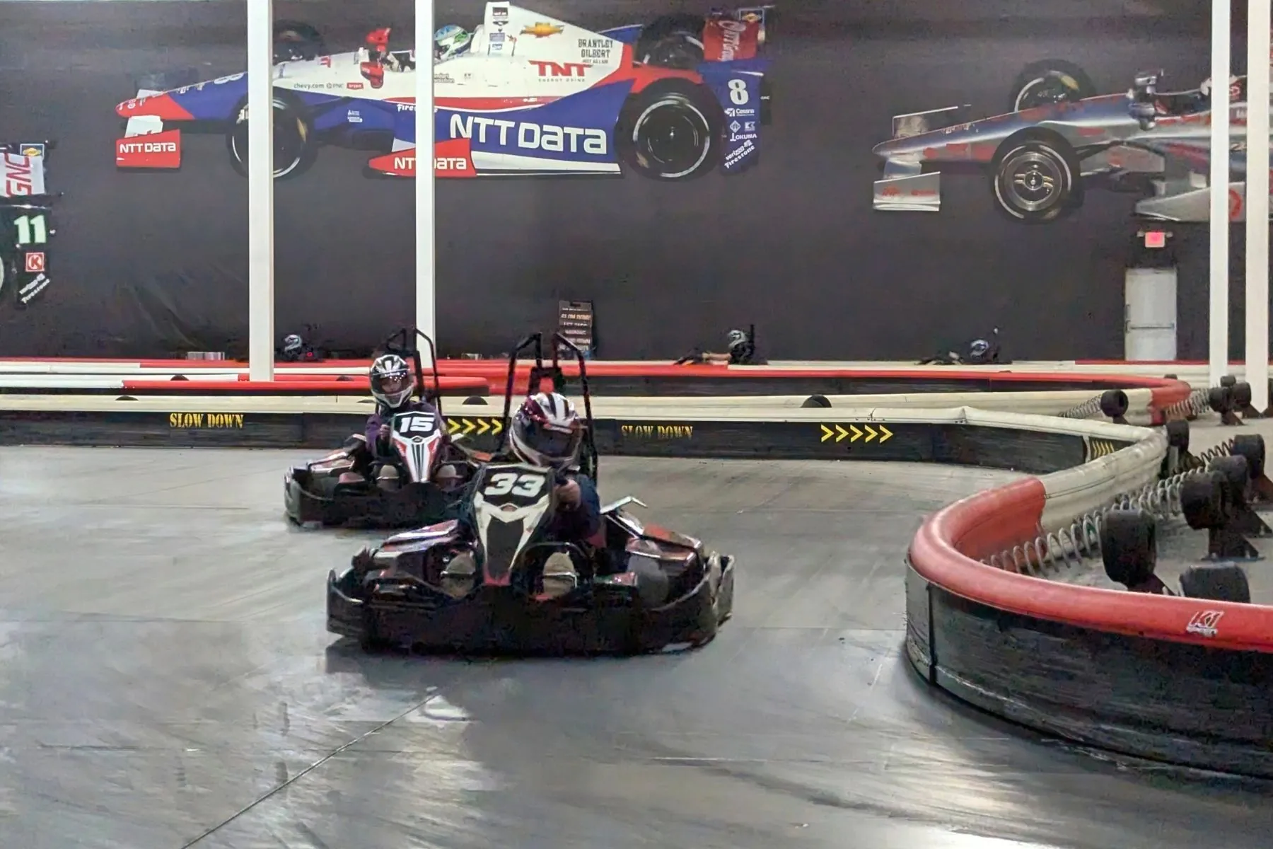 Two young drivers race go-karts on an indoor track.