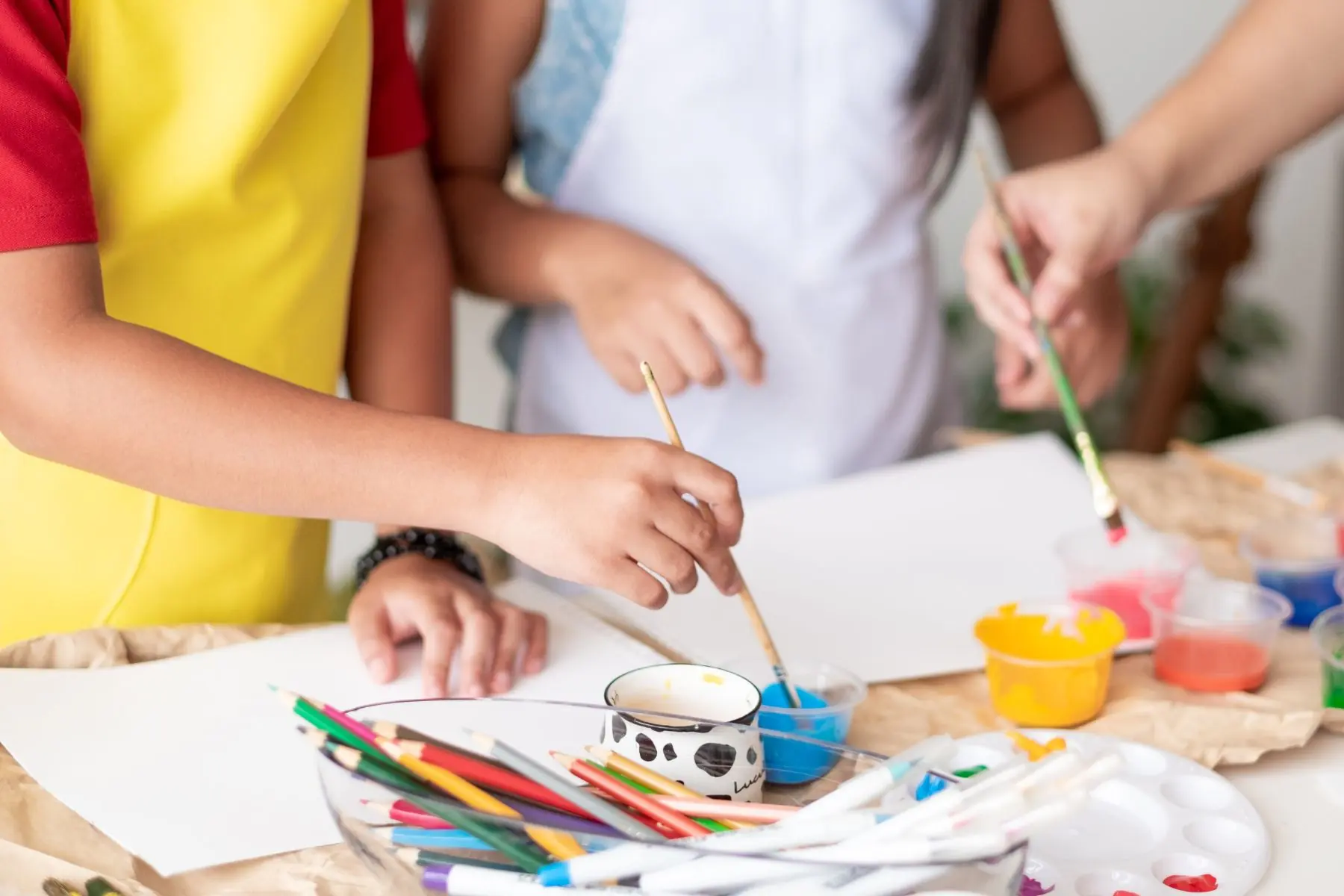 Children painting at a table with colorful paints, brushes, and art supplies during a hands-on art activity.