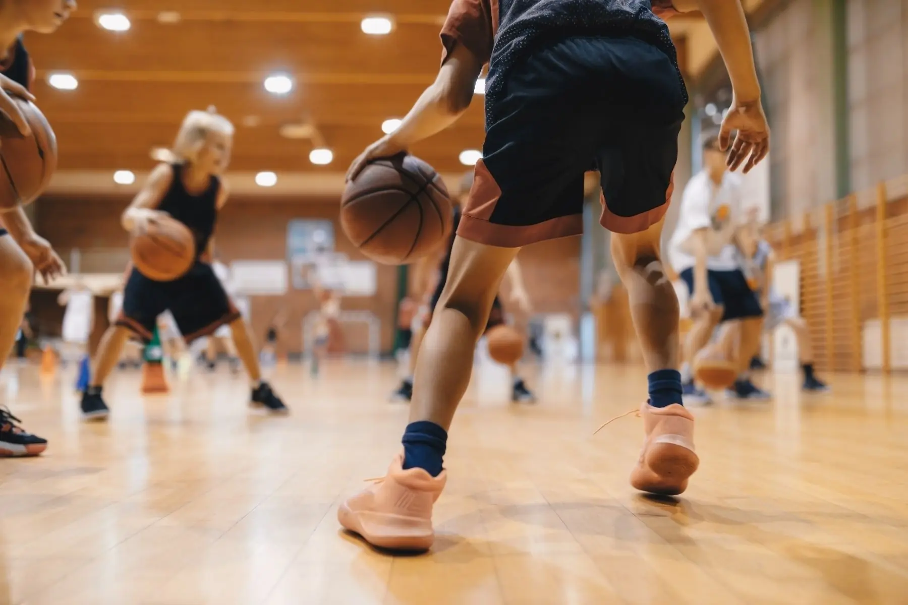 Young basketball players practicing dribbling drills on an indoor gym court during a group training session.