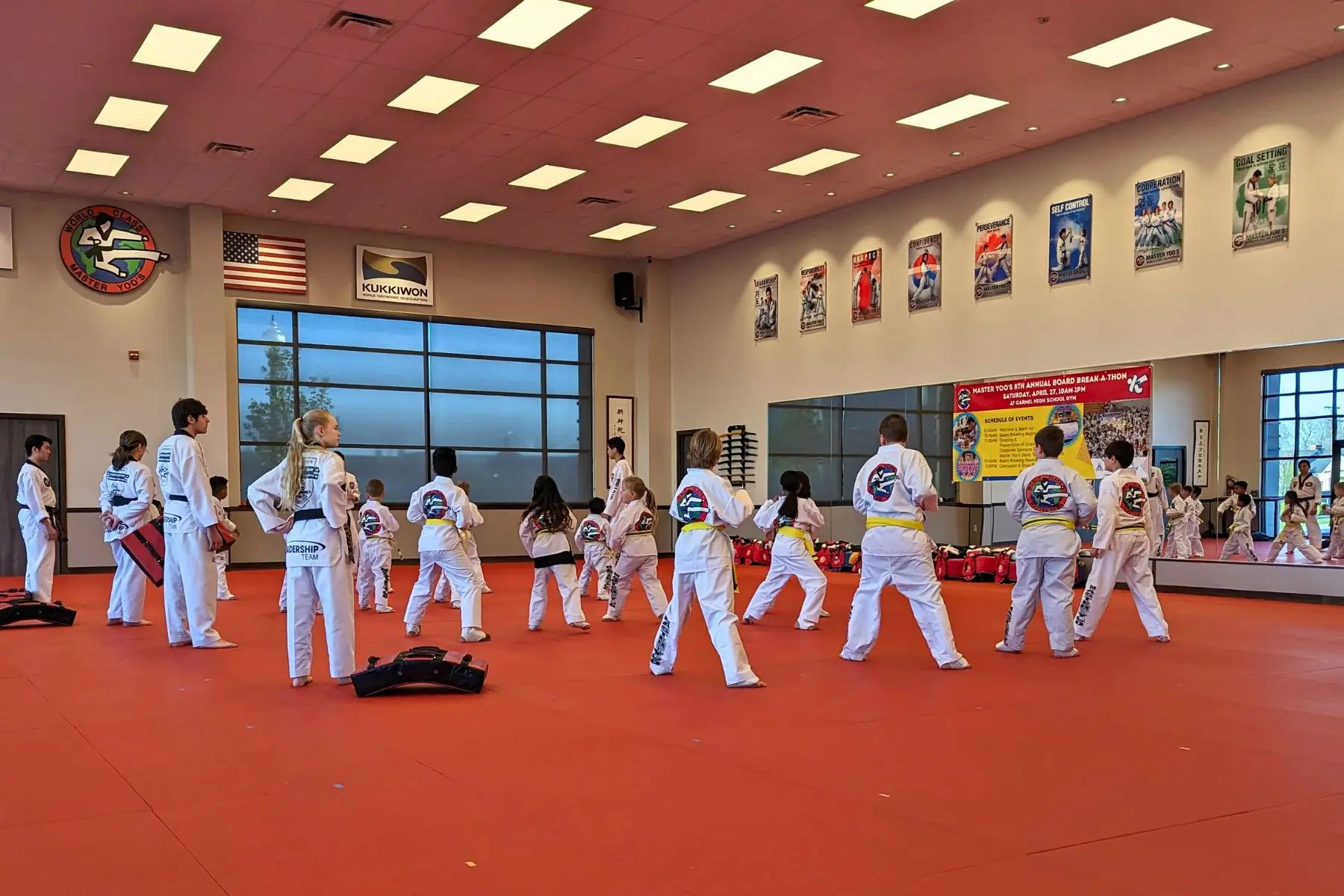 Kids martial arts class at Master Yoo’s Tae Kwon Do in Carmel featuring students in traditional dobok uniforms on red padded training mats.