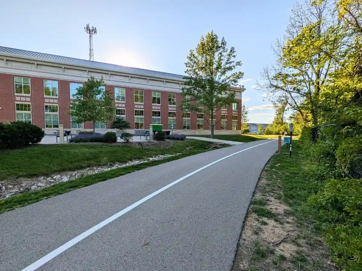 The paved asphalt path of the Big-4 Rail Trail passing directly alongside the brick building of Zionsville Town Hall in Zionsville, Indiana.