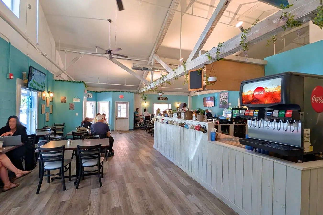 Our Place Coffee in Zionsville, showing a spacious café interior with teal walls, white vaulted ceilings, café tables, a long counter, and a self-serve drink station.