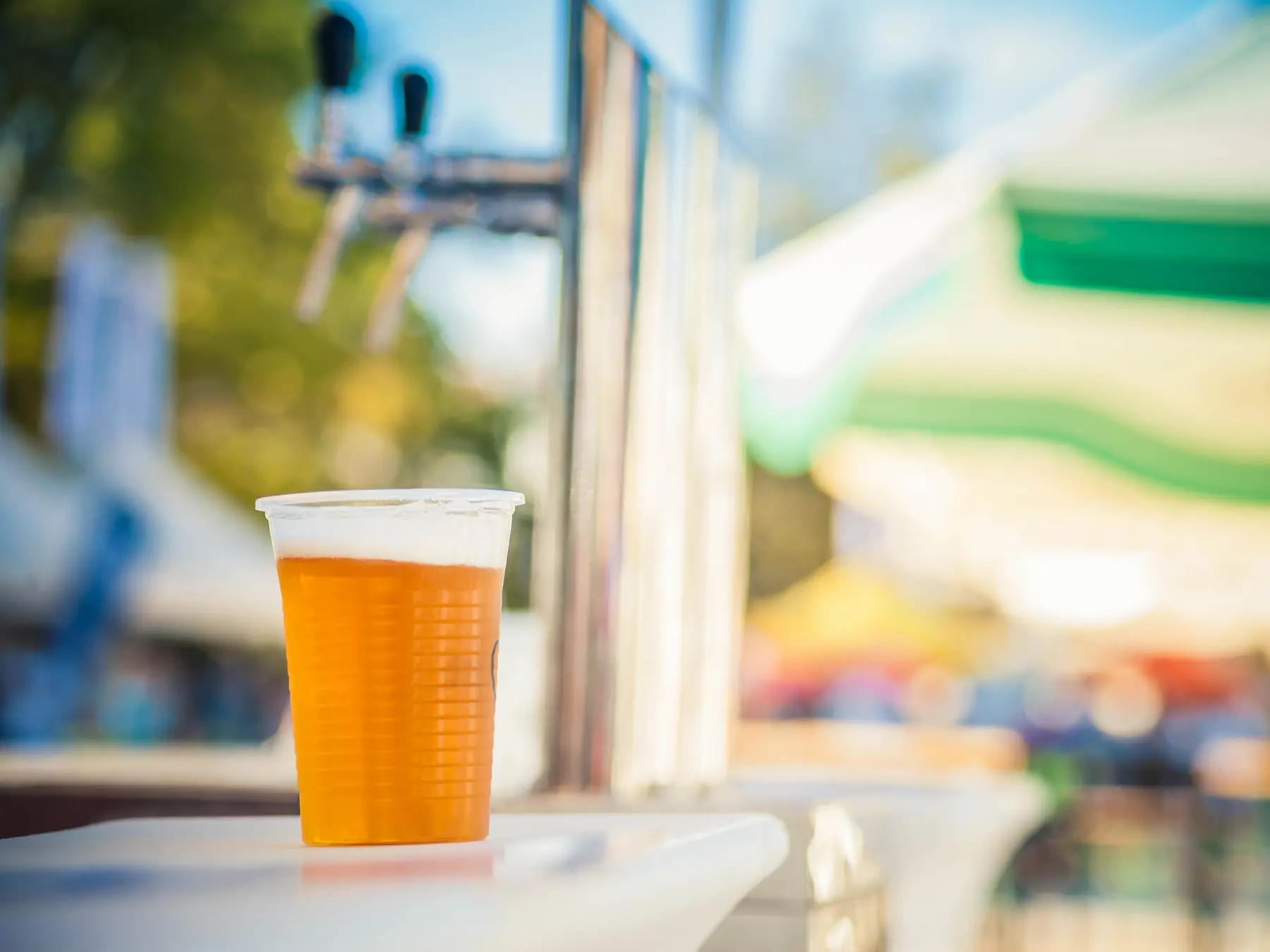 A clear plastic cup filled with light beer and foam, shown as an illustrative example of a refreshment for the downtown DORA guide.