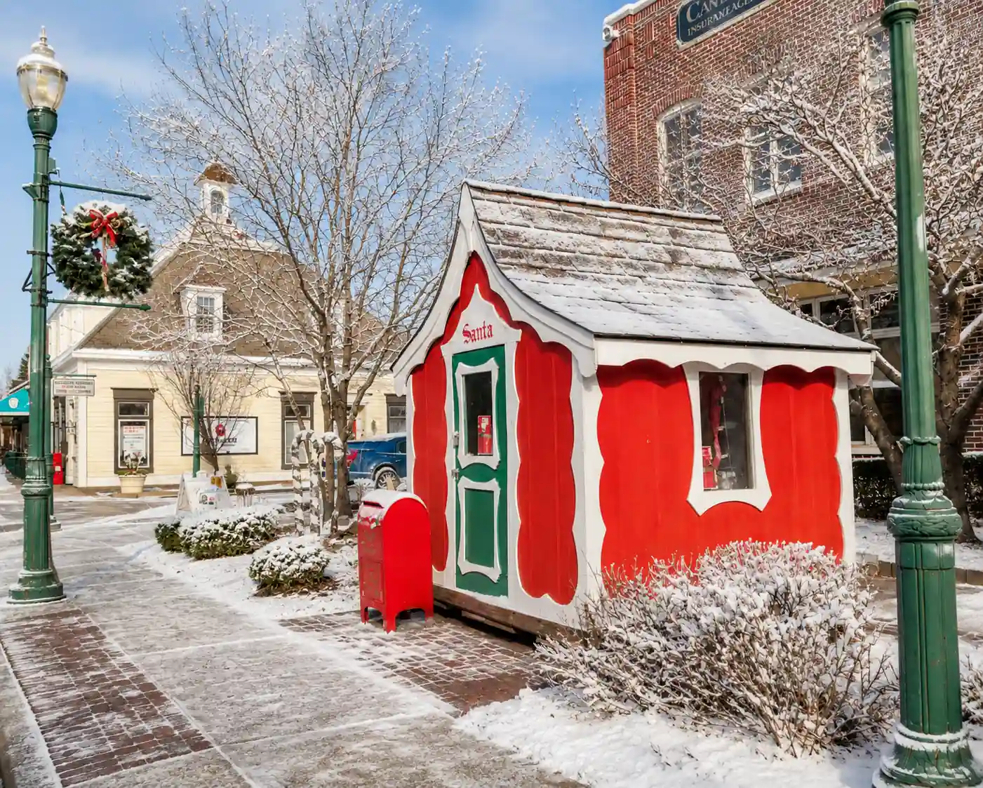 Small red and white Santa House with a red mailbox on a snow-dusted brick sidewalk at Cedar and Main Streets in downtown Zionsville.