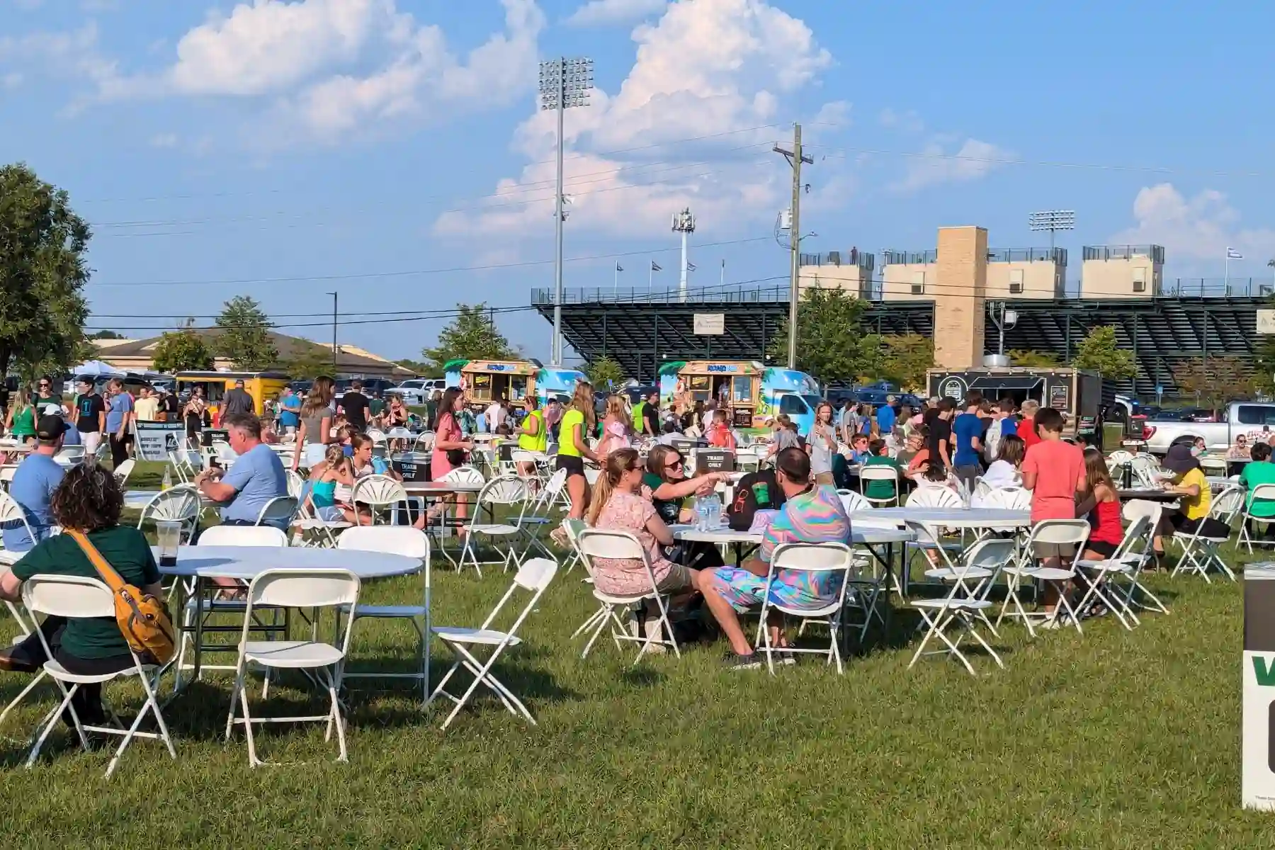 Outdoor dining area with white folding tables and food trucks lined up at Eagle Fest in Zionsville.