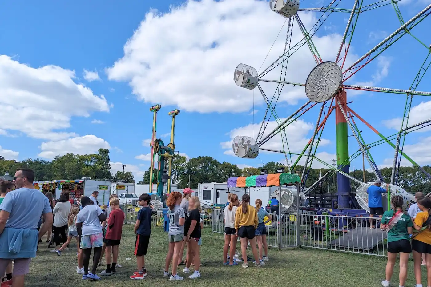 Visitors enjoying carnival rides, including a Ferris wheel and game booths, at the Zionsville Fall Festival.