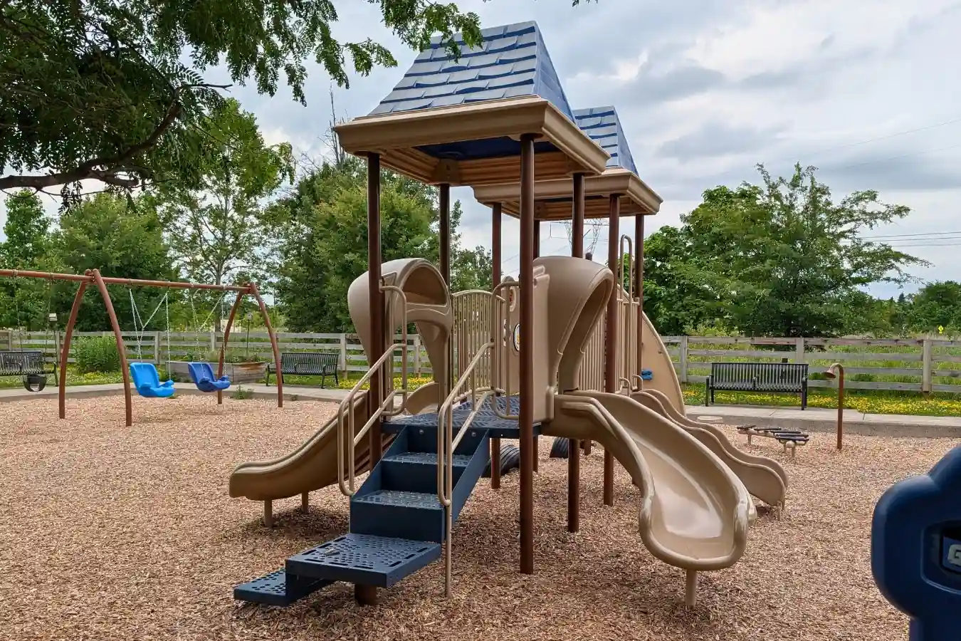 The main playground structure at Mulberry Fields Park includes blue-roofed towers, slides, stairs, and nearby swings on a wood-mulch play surface.