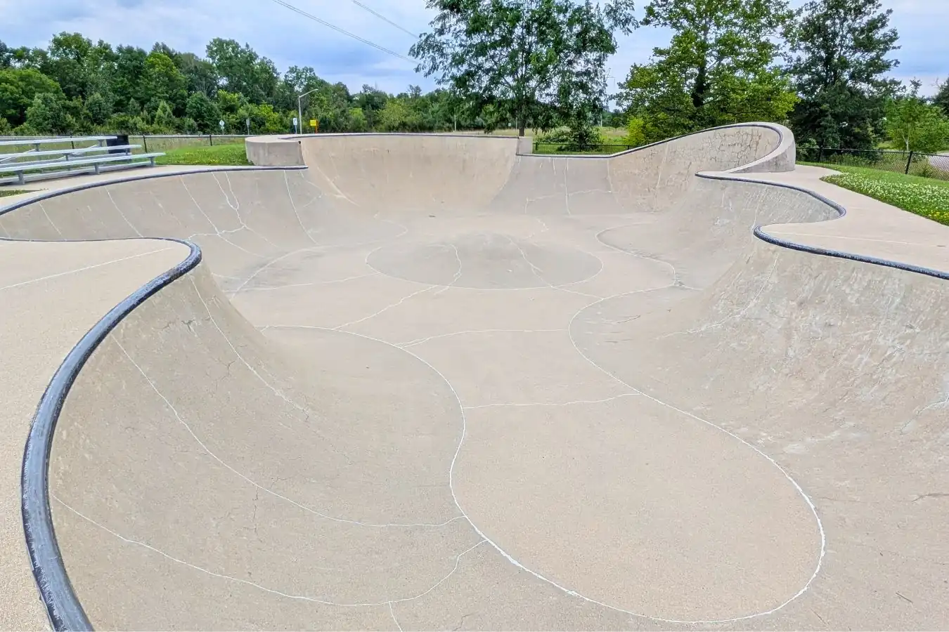 A wide view of the large concrete skate park bowl at Mulberry Fields Park in Zionsville, showing the metal coping, curved transition walls, and a central pump bump feature.
