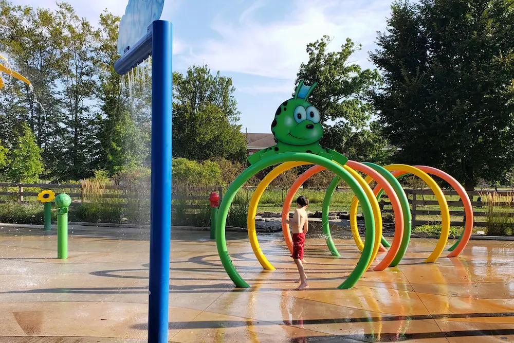 A child playing under the colorful spraying water arches and caterpillar feature at the Mulberry Fields splash pad in Zionsville.